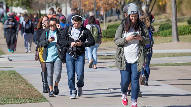 Students looking at cell phones while walking outside on campus.